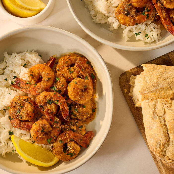 Two bowls of shrimp cooked with Mccormick Garlic And Olive Oil Seasoning Blend, 5.25 Oz, are served over white rice with a side of bread and lemon wedges.