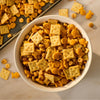 A white bowl is filled with a homemade snack mix of crackers and nuts, all tossed in a savory coating of Mccormick Garlic And Olive Oil Seasoning Blend, 5.25 Oz.