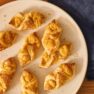A close-up, overhead shot shows several golden, twisted treacle tart pastries on a plate, generously sprinkled with Mccormick Harry Potter Treacle Tart Finishing Sugar, 3.43 Oz.