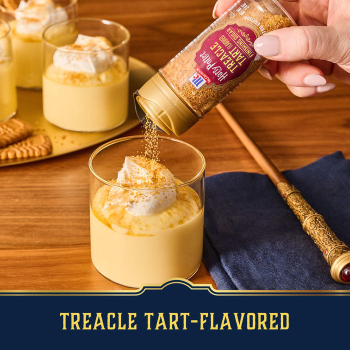 A hand sprinkles Mccormick Harry Potter Licorice Wand Finishing Sugar, 3.39 Oz, onto a creamy dip in a golden bowl, with a side of fresh strawberries.