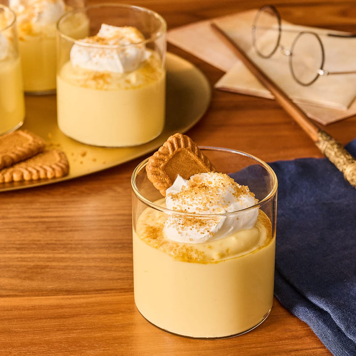 In a magical, Harry Potter-inspired setting, several glasses of creamy pudding are topped with whipped cream and a generous sprinkle of Mccormick Harry Potter Treacle Tart Finishing Sugar, 3.43 Oz.