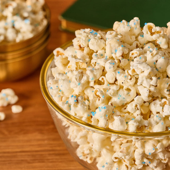 A glass bowl of white-coated popcorn is decorated with a sprinkle of Mccormick Harry Potter Drooble'S Best Blowing Gum Finishing Sugar, 3.36 Oz, creating a magical-looking snack.