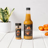 A bottle of Yellow Fruit hot sauce and a jar of Yellow Fruit seasoning are displayed on a white table with a plant and peppers.