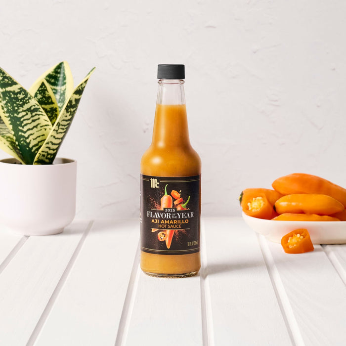 A bottle of Kumana Mango Habanero hot sauce is displayed with fresh habanero peppers and a potted plant.