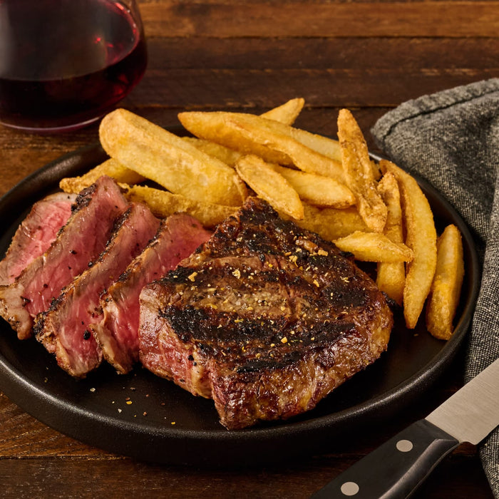 A perfectly cooked steak, seasoned with Mccormick Grill Mates Peppercorn And Worcestershire Seasoning Cracked 2.75 Oz, is sliced and served on a black plate with steak fries and a glass of red wine.