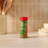 A bottle of Mccormick Chimichurri Flavored Seasoning, 2.47 Oz sits on a light-colored marble countertop in a kitchen setting, with a utensil holder and plates in the background.
