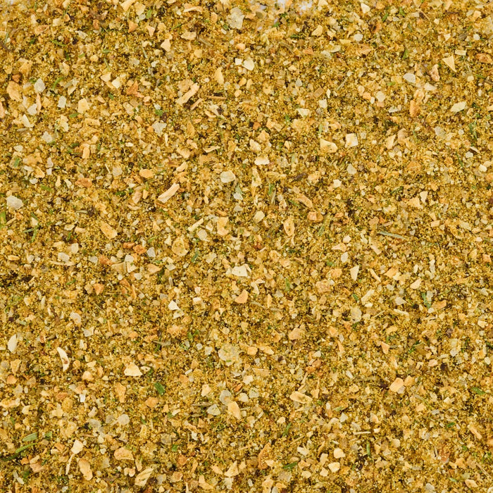 A close-up, top-down view reveals the texture of Mccormick Caramelized Onion Seasoning, 4.66 Oz, showing a blend of yellow powder, dried green herbs, and dehydrated onion flakes.