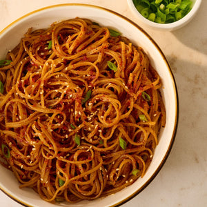 A close-up, overhead view of a bowl of noodles generously seasoned with Mccormick Chili Garlic Seasoning, 5.22 Oz, and garnished with sesame seeds and fresh green onions.