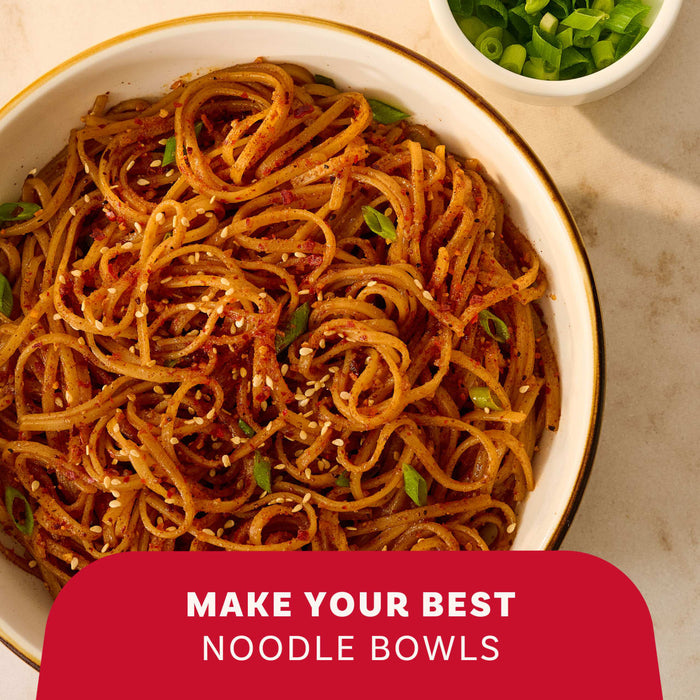 A close-up, overhead shot shows a white bowl filled with noodles tossed with sesame seeds, green onions, and Mccormick Chili Garlic Seasoning, 5.22 Oz, with a red banner at the bottom that reads, Make Your Best Noodle Bowls.