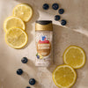 A bottle of Mccormick Blueberry And Lemon Finishing Sugar, 3.43 Oz, is styled on a marbled surface, artfully arranged with fresh lemon slices and scattered blueberries to showcase its flavor profile.