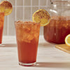 A tall glass of iced tea is garnished with a lemon wheel and a sprinkle of Mccormick Blueberry And Lemon Finishing Sugar, 3.43 Oz, with a pitcher of tea in the background.
