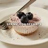A mini blueberry cheesecake on a white plate demonstrates a serving suggestion for Mccormick Blueberry And Lemon Finishing Sugar, 3.43 Oz, which is sprinkled over the top.