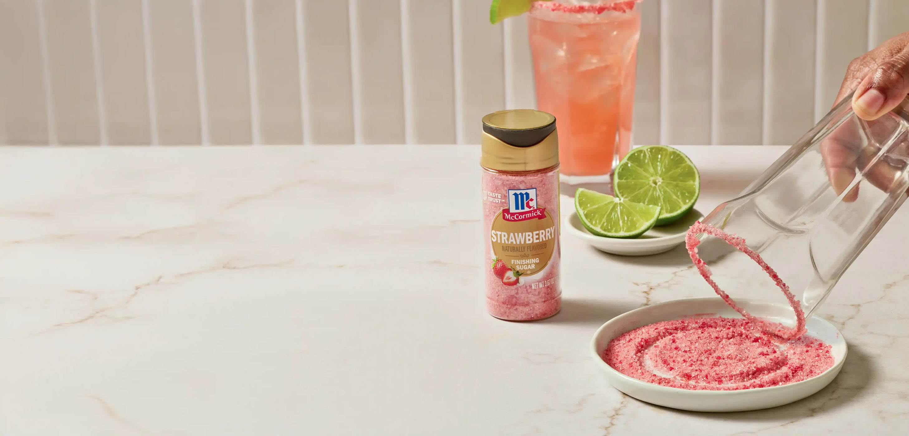 Strawberry finishing sugar bottle with a hand holding a glass that is being rimmed in the pink sugar