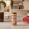 A bottle of Mccormick Cranberry Finishing Sugar, 3.43 Oz sits on a white kitchen counter in a festive holiday setting with a French press and red plates.