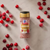 A bottle of Mccormick Cranberry Finishing Sugar, 3.43 Oz is centered on a marble surface surrounded by fresh and sugared cranberries.