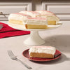 A slice of moist yellow cake topped with a thick layer of creamy white frosting and a delicate dusting of Mccormick Cranberry Finishing Sugar 3.43 Oz sits on a red plate next to a silver fork.