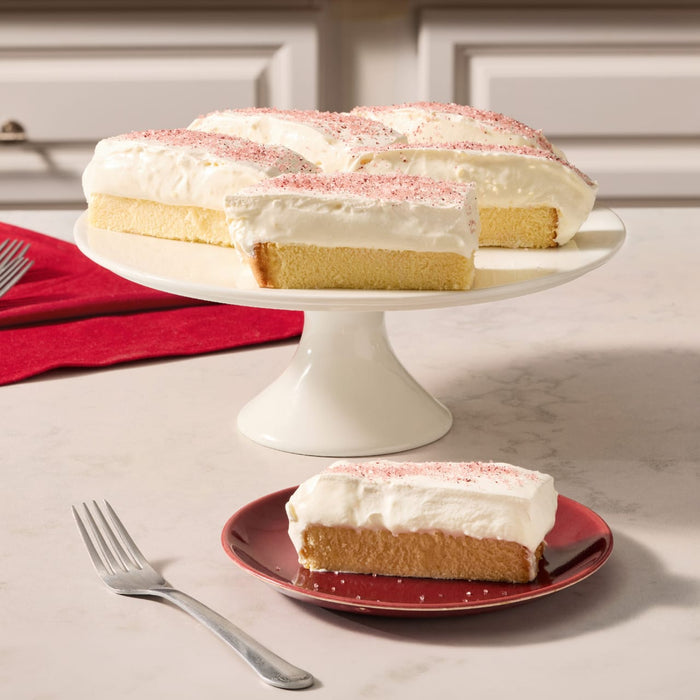 A slice of moist yellow cake topped with a thick layer of creamy white frosting and a delicate dusting of Mccormick Cranberry Finishing Sugar 3.43 Oz sits on a red plate next to a silver fork.