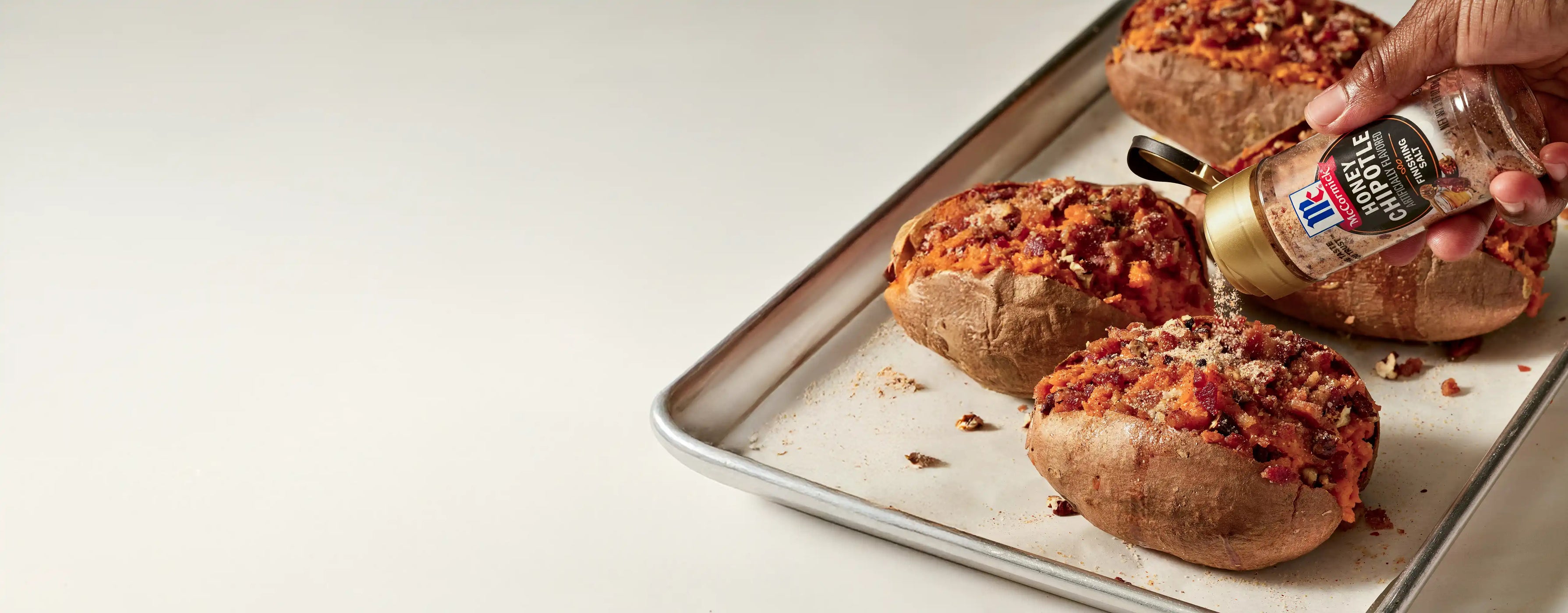 sweet potatoes being topped with honey chipotle finishing salt on a tray