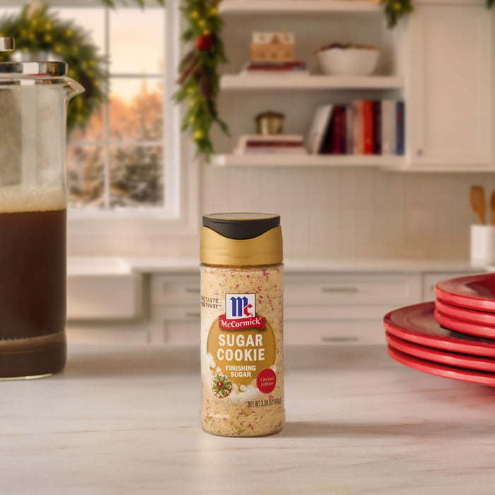 A bottle of Mccormick Sugar Cookie Finishing Sugar, 3.39 Oz sits on a white marble countertop in a cozy kitchen decorated for the holidays.