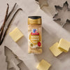 A bottle of Mccormick Sugar Cookie Finishing Sugar, 3.39 Oz is centered on a marble surface surrounded by festive baking essentials like vanilla beans, pats of butter, and holiday cookie cutters.