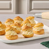 A white platter holds several golden cream puffs filled with a light swirl of frosting and topped with a dusting of Mccormick Sugar Cookie Finishing Sugar, 3.39 Oz.