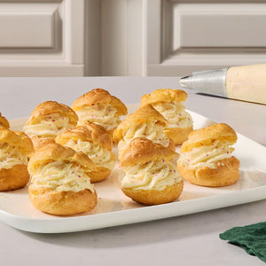 A white platter holds several golden cream puffs filled with a light swirl of frosting and topped with a dusting of Mccormick Sugar Cookie Finishing Sugar, 3.39 Oz.