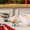 A festive dessert scene features a scoop of vanilla ice cream topped with a swirl of whipped cream and a dusting of Mccormick Sugar Cookie Finishing Sugar 3.39 Oz in a silver bowl.