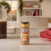 A bottle of Mccormick Dulce De Leche Finishing Sugar, 3.43 Oz sits on a white marble countertop in a cozy kitchen decorated for the holidays.
