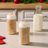 Two glasses of iced coffee topped with thick foam and a sprinkle of Mccormick Dulce De Leche Finishing Sugar 3.43 Oz sit on a counter next to a bottle of milk.