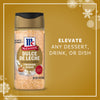 A bottle of Mccormick Dulce De Leche Finishing Sugar, 3.43 Oz is displayed against a festive gold background with snowflakes to show how it can elevate any dessert, drink, or dish.