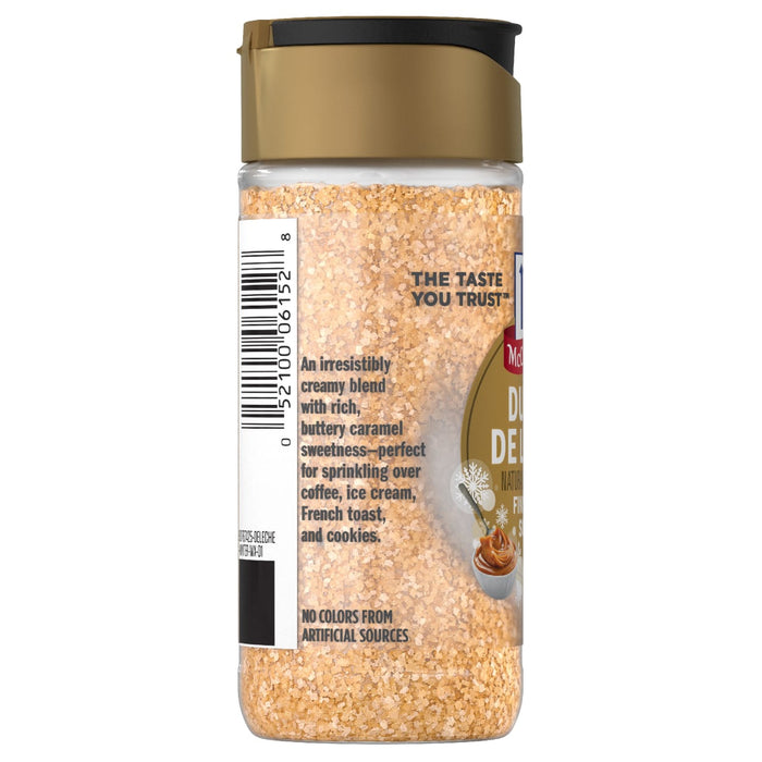 A side view of a clear bottle of Mccormick, 3.43 Oz Dulce de Leche Naturally Flavored Finishing Sugar showing the tan granules and product description.