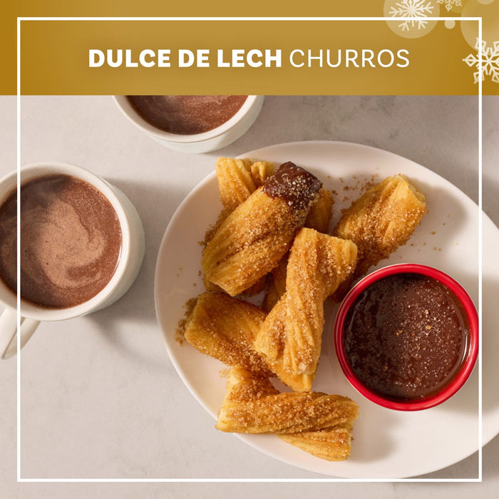 A plate of golden brown churros and a small bowl of dipping sauce are generously coated with Mccormick Dulce De Leche Finishing Sugar, 3.43 Oz, served alongside two mugs of hot chocolate.