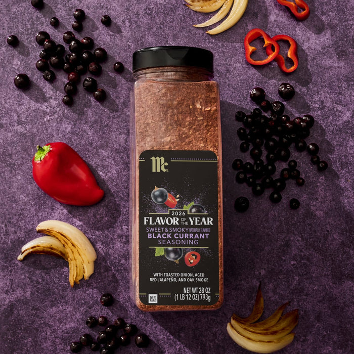 A jar of McCormick Flavor of the Year 2026 Sweet &amp; Smoky Naturally Flavored Black Currant Seasoning is displayed with black currants, red peppers, and toasted onions.