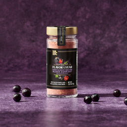A jar of McCormick 2026 Flavor of the Year Sweet &amp; Smoky Naturally Flavored Black Currant Seasoning is surrounded by black currants.