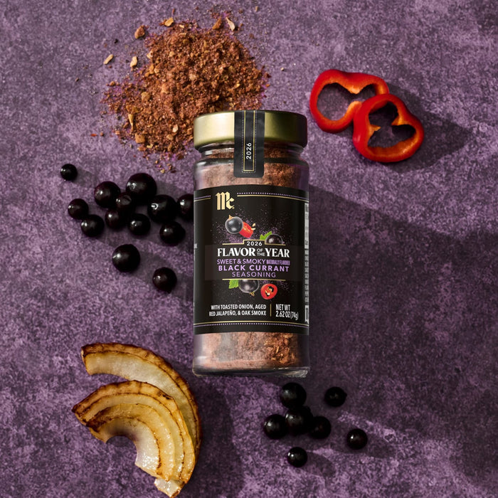 A jar of McCormick 2026 Flavor of the Year Sweet &amp; Smoky Naturally Flavored Black Currant Seasoning is displayed with black currants, red pepper slices, toasted onion, and a pile of seasoning.