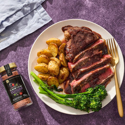 A plate of steak, potatoes, and broccolini is displayed with a jar of McCormick 2026 Flavor of the Year Sweet &amp; Smoky Naturally Flavored Black Currant Seasoning.
