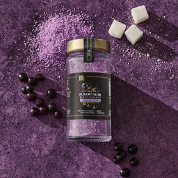 A jar of McCormick Flavor of the Year 2026 Black Currant Finishing Sugar is displayed with black currants, sugar cubes, and purple sugar crystals on a purple surface.