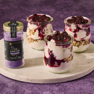 A jar of McCormick Flavor of the Year 2026 Black Currant Finishing Sugar sits next to three small glass jars filled with a layered dessert.