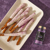 A white platter holds pretzel rods dipped in white chocolate and McCormick Flavor of the Year Black Currant Finishing Sugar, next to a jar of the finishing sugar.