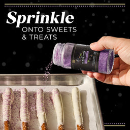 A hand sprinkles McCormick Flavor of the Year 2026 Black Currant Finishing Sugar onto white chocolate-covered pretzel rods.