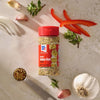 A bottle of Mccormick Spicy Sicilian Style Seasoning, 1.62 Oz, is featured in a top-down view, surrounded by fresh ingredients like garlic, sliced red pepper, and oregano, along with a measuring spoon filled with the seasoning blend.
