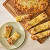 A top-down view shows delicious cheesy garlic bread, seasoned with Mccormick Spicy Sicilian Style Seasoning, 1.62 Oz, cut into sticks and served on a wooden board and a light green plate.