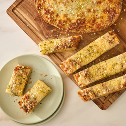 A top-down view shows delicious cheesy garlic bread, seasoned with Mccormick Spicy Sicilian Style Seasoning, 1.62 Oz, cut into sticks and served on a wooden board and a light green plate.
