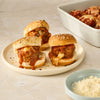 Three meatball sliders, made with Mccormick Spicy Sicilian Style Seasoning, 1.62 Oz, are arranged on a plate with a side of grated cheese.