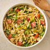 A large white bowl of pasta salad with tomatoes, mozzarella, and arugula, seasoned with Mccormick Spicy Sicilian Style Seasoning, 1.62 Oz, is shown from above with wooden salad servers nearby.