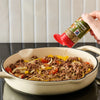 A hand sprinkles Mccormick Savory Herb Parmesan Seasoning, 2.5 Oz over a skillet of cooked ground beef, onions, and peppers.