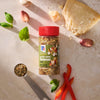 A bottle of Mccormick Savory Herb Parmesan Seasoning, 2.5 Oz is displayed in a top-down view with fresh ingredients like parmesan cheese, garlic, basil, and red pepper, along with a measuring spoon of the seasoning.