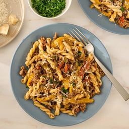A delicious plate of gemelli pasta with ground meat and yellow peppers is garnished with fresh parsley and cheese, showcasing a meal made with Mccormick Savory Herb Parmesan Seasoning, 2.5 Oz.