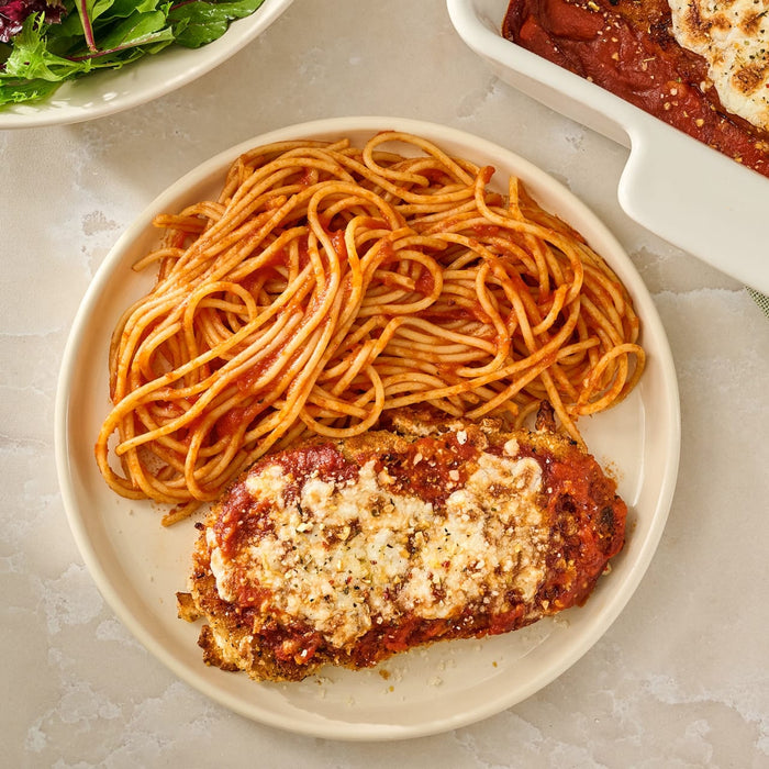 A plate of chicken parmesan and spaghetti, with the chicken topped with melted cheese and a sprinkle of Mccormick Savory Herb Parmesan Seasoning, 2.5 Oz.