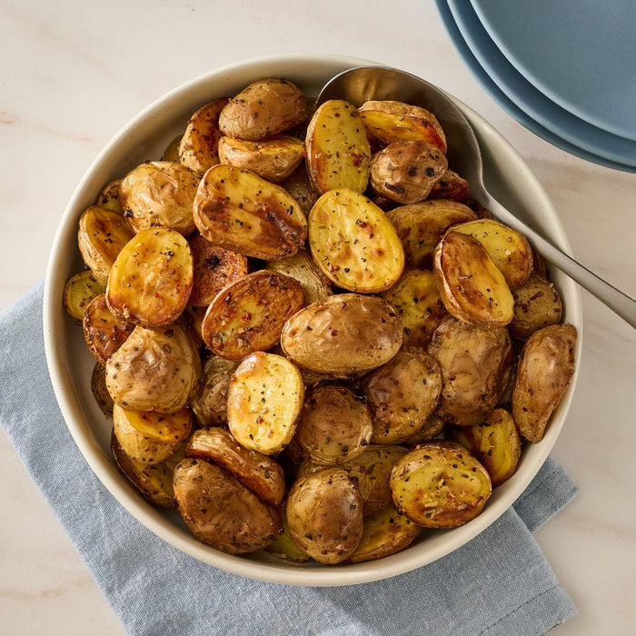 A white bowl filled with roasted new potatoes, seasoned with Mccormick Savory Herb Parmesan Seasoning, 2.5 Oz, sits on a blue napkin.